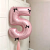 A pink foil balloon shaped like the number 5 with a black bow, hanging on a white door.
