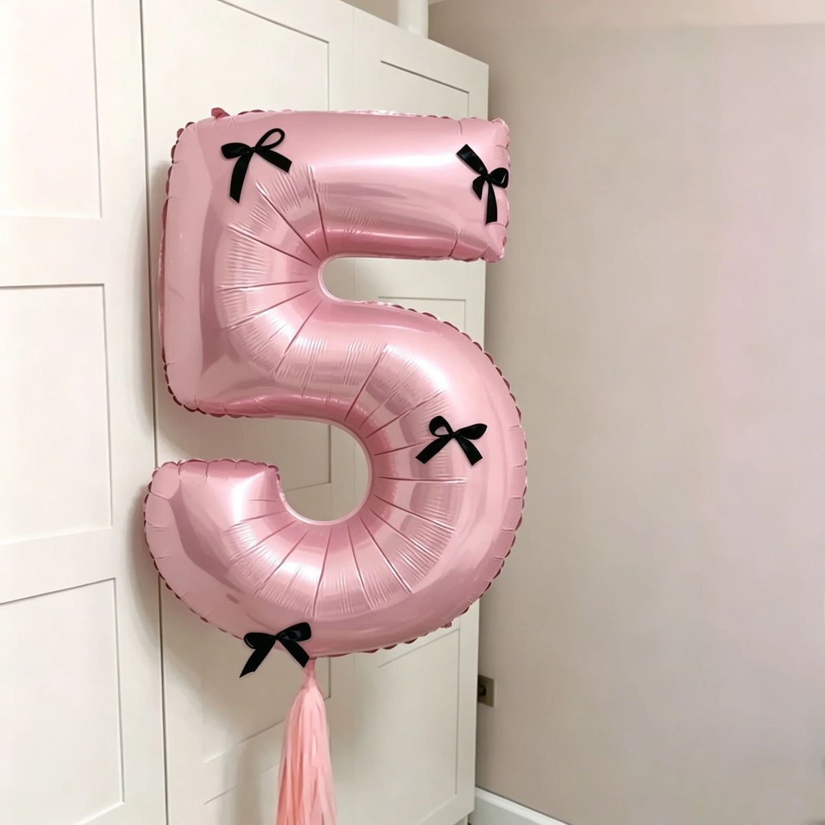 A pink foil balloon shaped like the number 5 with a black bow, hanging on a white door.