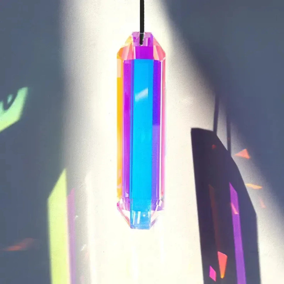 A vertical pendant featuring a prismatic crystal with rainbow colors hanging against a bright background.