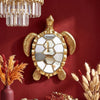 Golden sea turtle resin wall decor mirror mounted on a deep red wall with a crystal chandelier above.