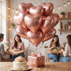 A bouquet of pink heart-shaped foil balloons is displayed on a wooden table in a bright indoor setting.