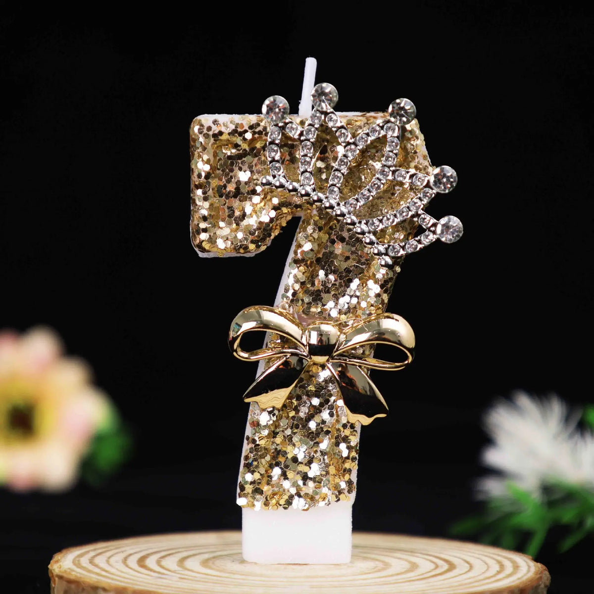 Gold glitter number cake topper candles featuring a rhinestone bow on a wooden slice.