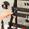A hand is shown placing a red earring onto a black wooden multilayer organizer for jewelry display.