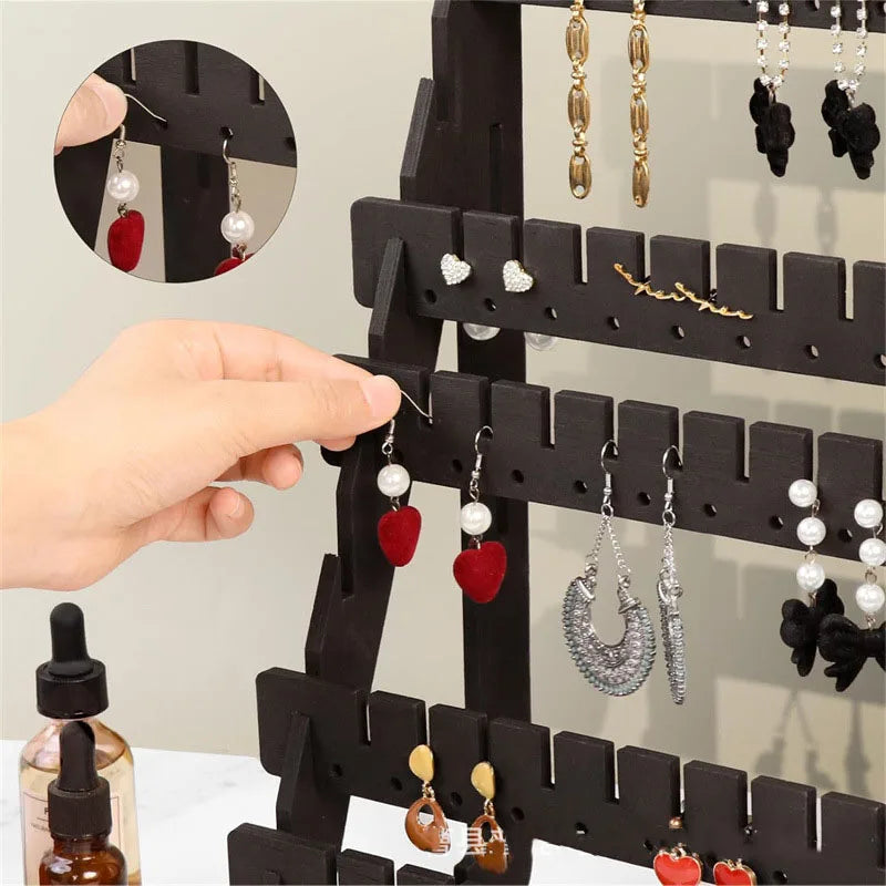 A hand is shown placing a red earring onto a black wooden multilayer organizer for jewelry display.