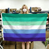 A person holds up a horizontal Pride flag banner with six horizontal stripes of green, white, light blue, medium blue, and pu