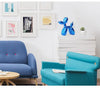 A teal blue resin balloon dog sculpture decor item displayed on a white cabinet with framed art.