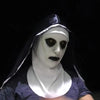 A white latex mask of a nun with a black headscarf and dark makeup against a black background.