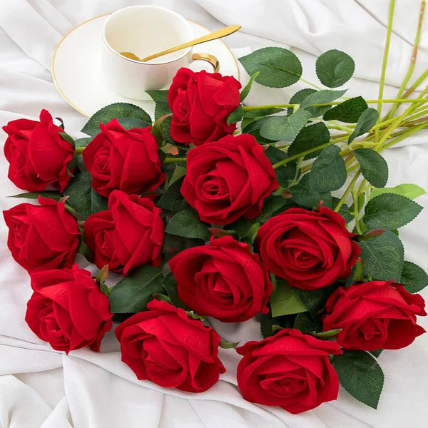 A bouquet of deep red velvet artificial roses with green leaves and a white cup on a white cloth.