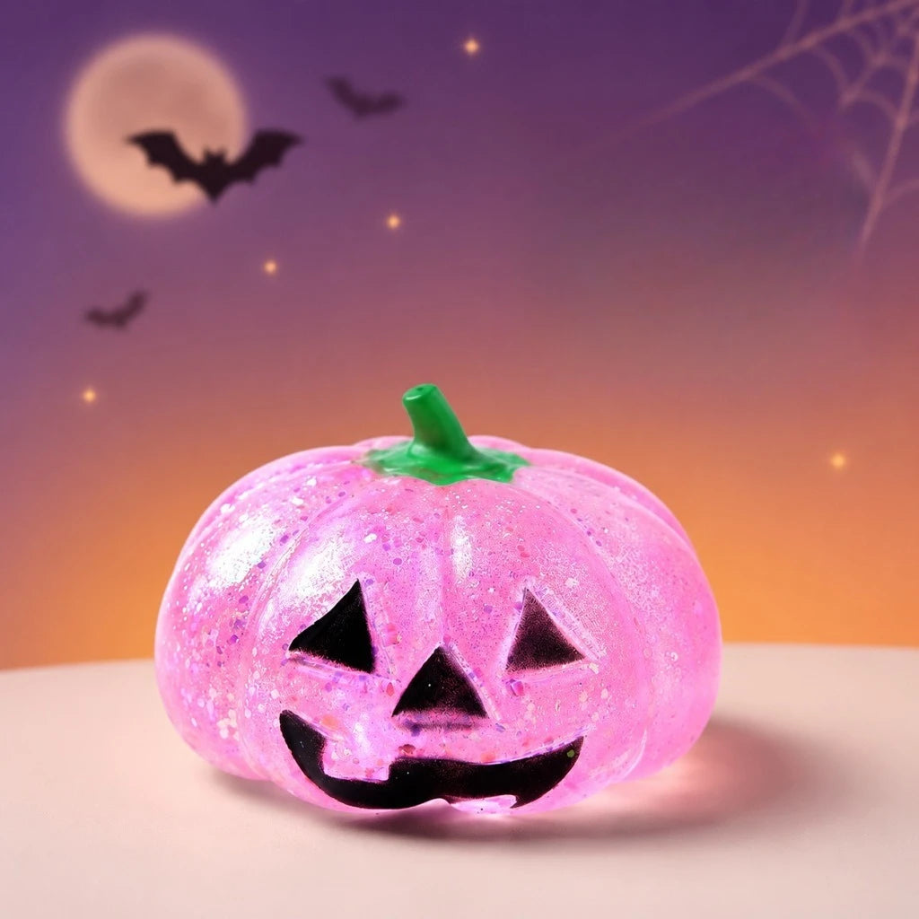 A bright pink Halloween pumpkin stress ball with a carved face sits against a purple and orange background with bats flying.