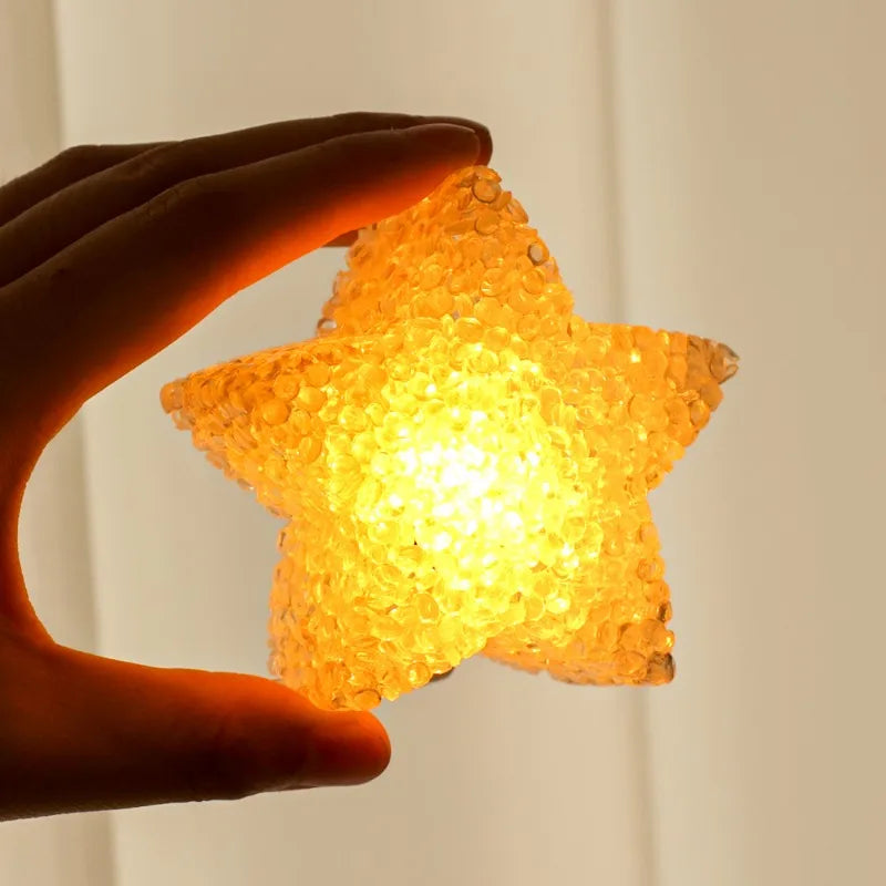A hand holds an LED star-shaped light emitting a warm yellow glow.