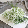 A bouquet of artificial white gypsophila flowers displayed on a white rectangular plate against a gray fabric background.