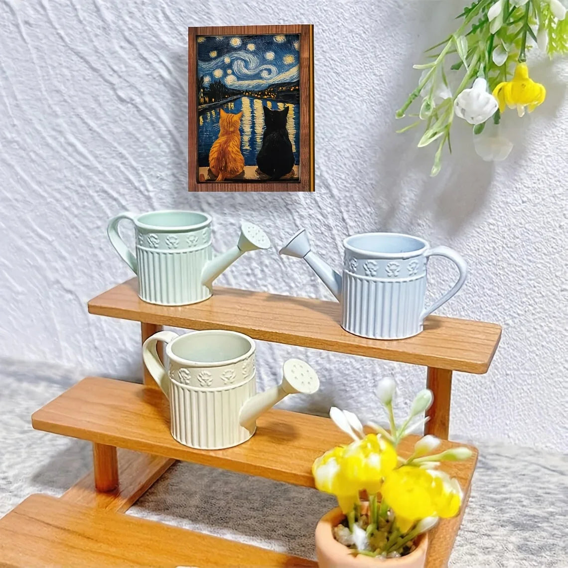 A wooden art print featuring a starry night sky with cats, displayed next to ceramic teapots and a watering can.