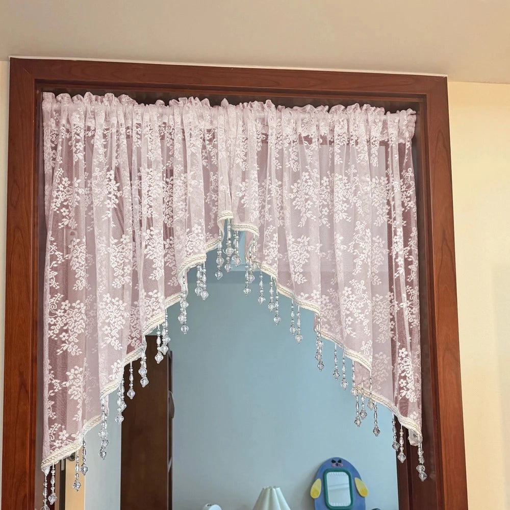 A sheer pink beaded lace valance curtain draped over a wooden mirror frame.