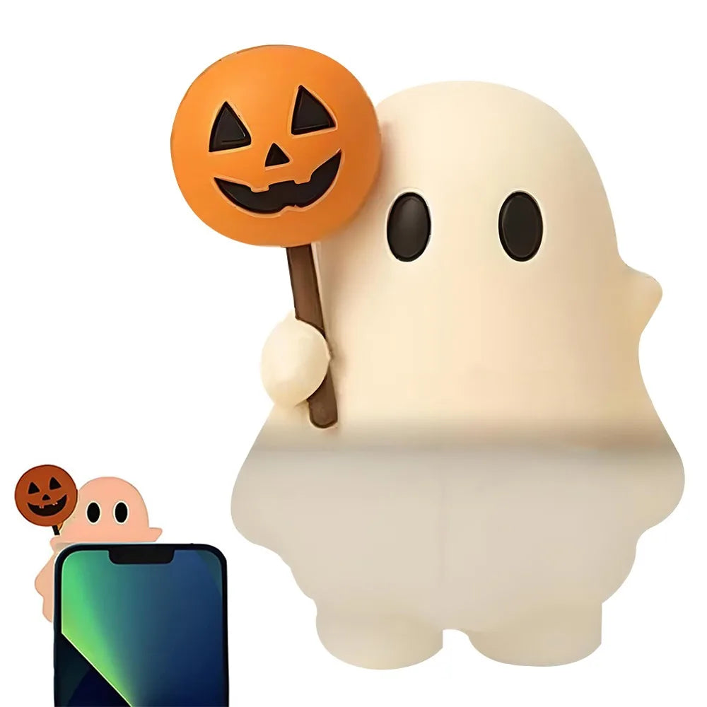 A white ghost phone decoration charm with an orange Jack-o'-lantern face attached, next to a smartphone.