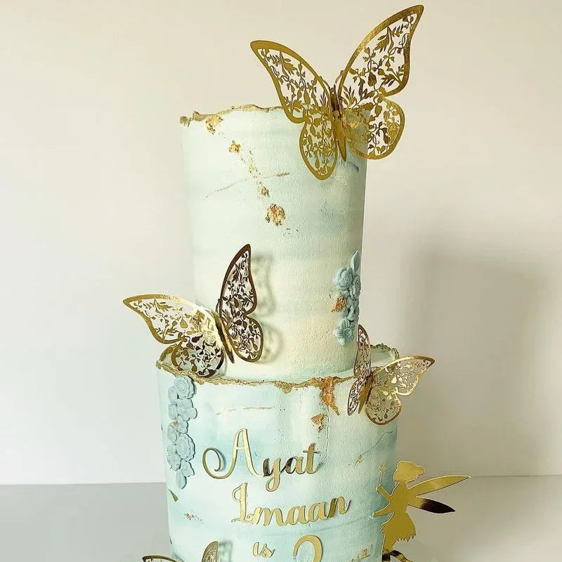 A two-tiered light blue cake decorated with gold butterfly toppers and floral accents.