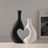 A pair of modern heart-shaped ceramic vases in matte black and white sitting on a light surface.