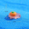 An orange and pink glow-in-the-dark fruit turtle resin charm resting on a blue glitter surface.