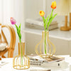 A handcrafted gold iron hollow vase holds a single yellow tulip in a modern interior setting.