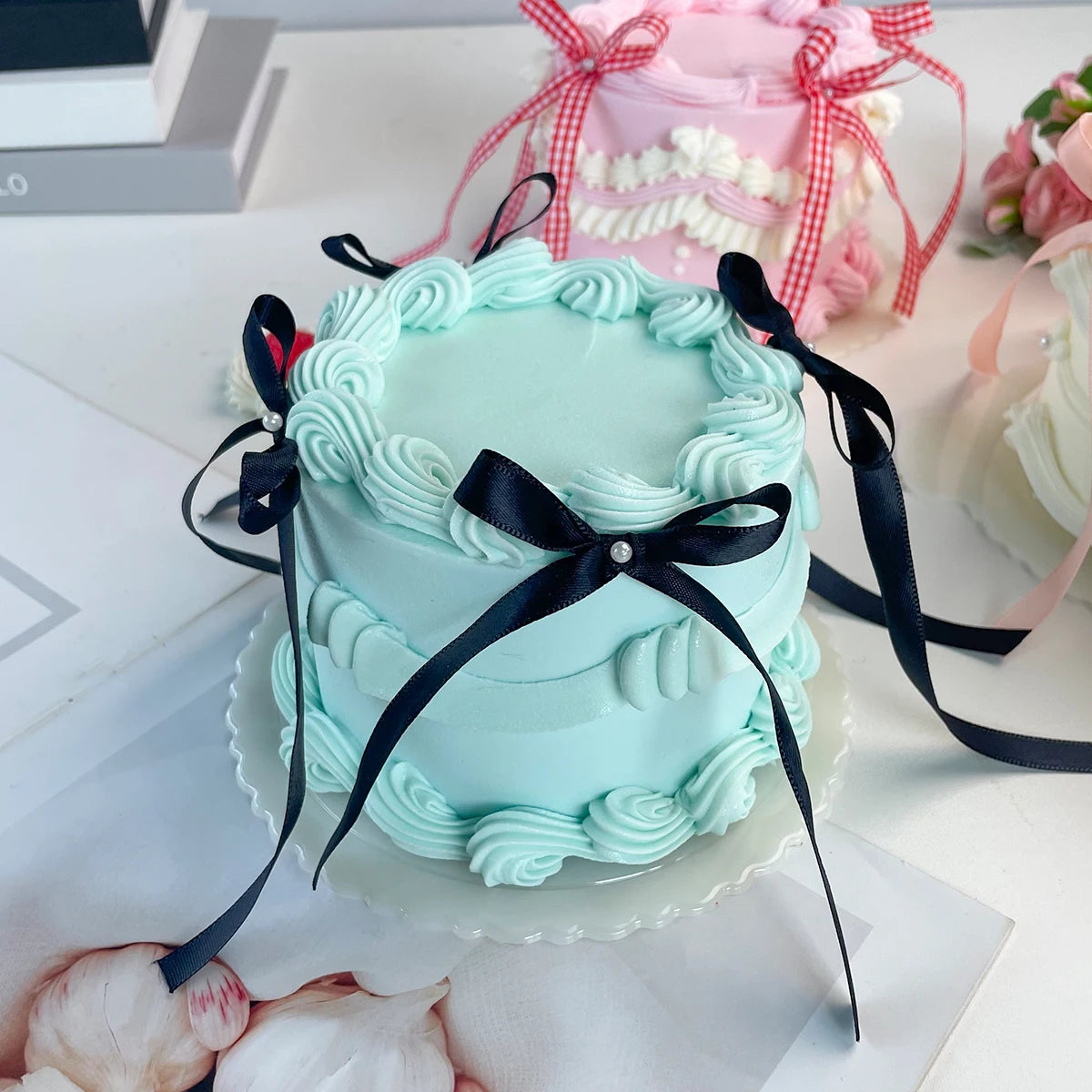A light blue decorative fake cake with ruffled frosting and black ribbons is displayed on a white plate.