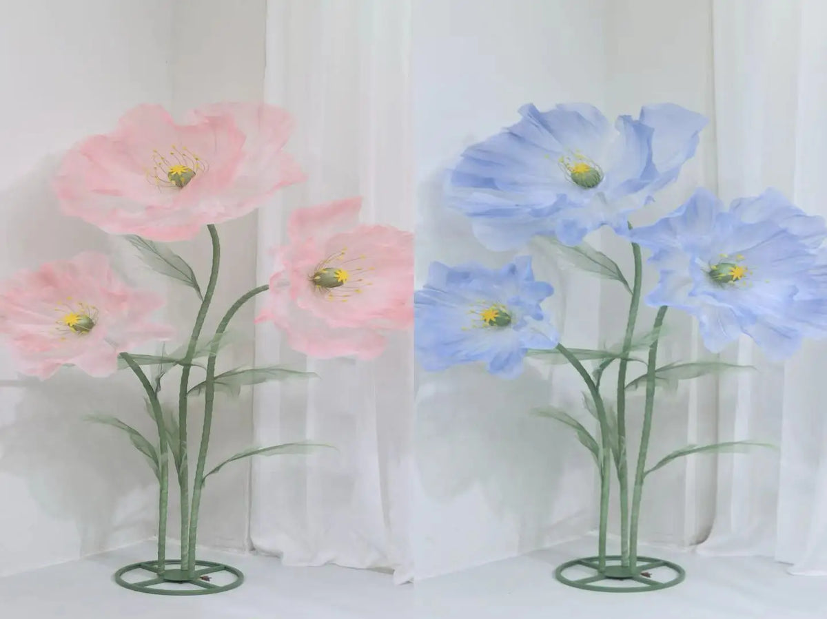 A pair of large artificial silk poppy flowers in pink and blue are displayed against a white background.