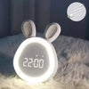 A white, rabbit-shaped LED night light alarm clock is illuminated on a fluffy surface.