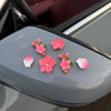 A collection of pink and white 3D peach blossom ornaments displayed on a gray car dashboard.