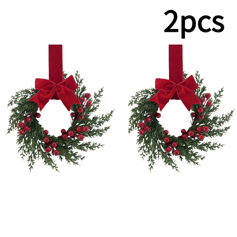 Two artificial Christmas wreaths featuring green foliage, red berries, and a large red velvet bow.