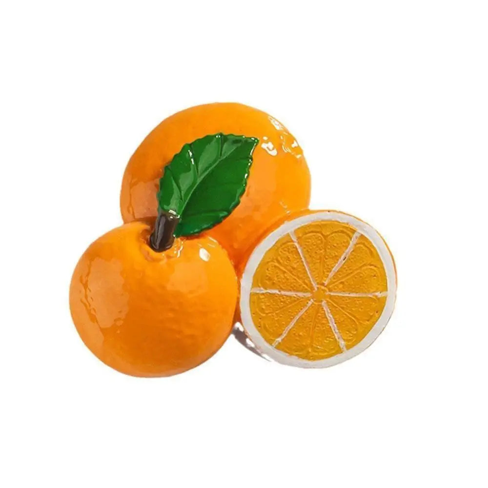 A bright orange peach with a green leaf next to a slice of orange fruit magnet.