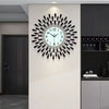 A modern minimalist metal wall clock with a white face and black spokes is mounted on a light gray wall.