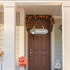 A wooden welcome sign with a wreath and a 'Welcome' plaque hangs above a brown door on a porch.