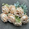 A bouquet of nine realistic silk roses in soft peach and cream tones arranged on a gray fabric.