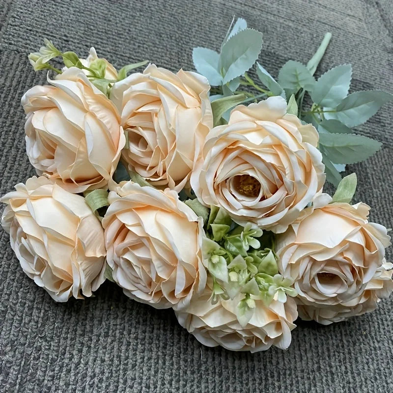 A bouquet of nine realistic silk roses in soft peach and cream tones arranged on a gray fabric.