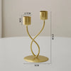 A gold-colored iron candle holder with a cylindrical top and a curved stand, shown against a light background.
