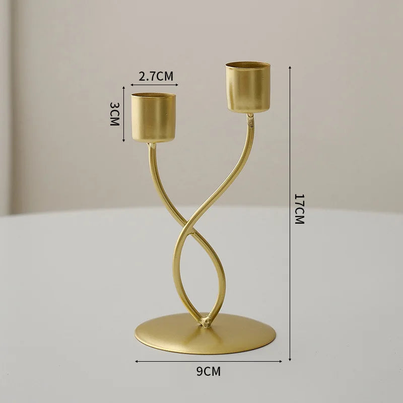 A gold-colored iron candle holder with a cylindrical top and a curved stand, shown against a light background.