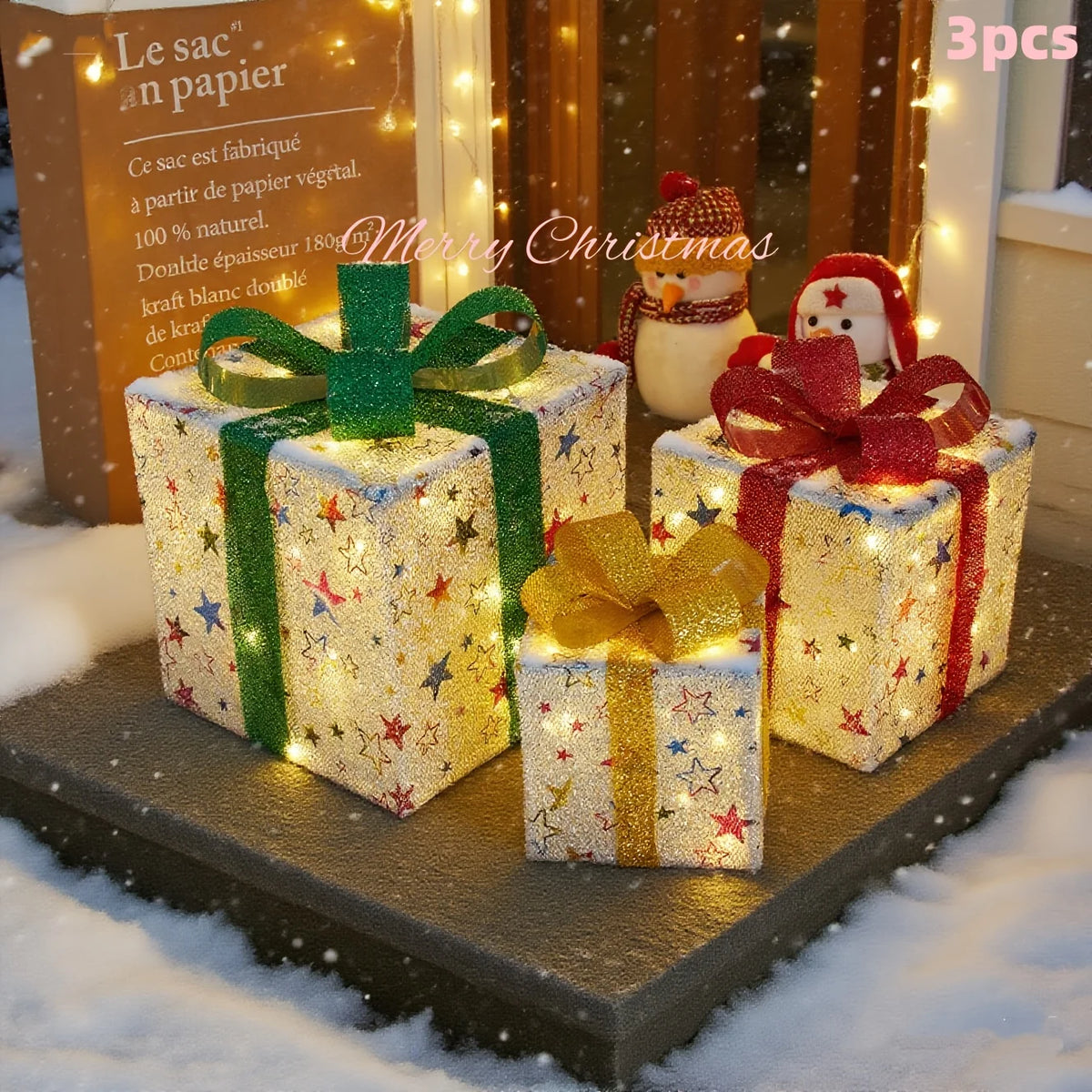Three light-up Christmas gift boxes wrapped in gold and green paper with festive ribbons displayed on a snowy surface.