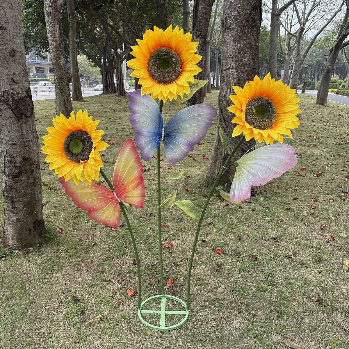 A set of giant silk sunflowers with flexible stems and a metal base displayed on a grassy area.