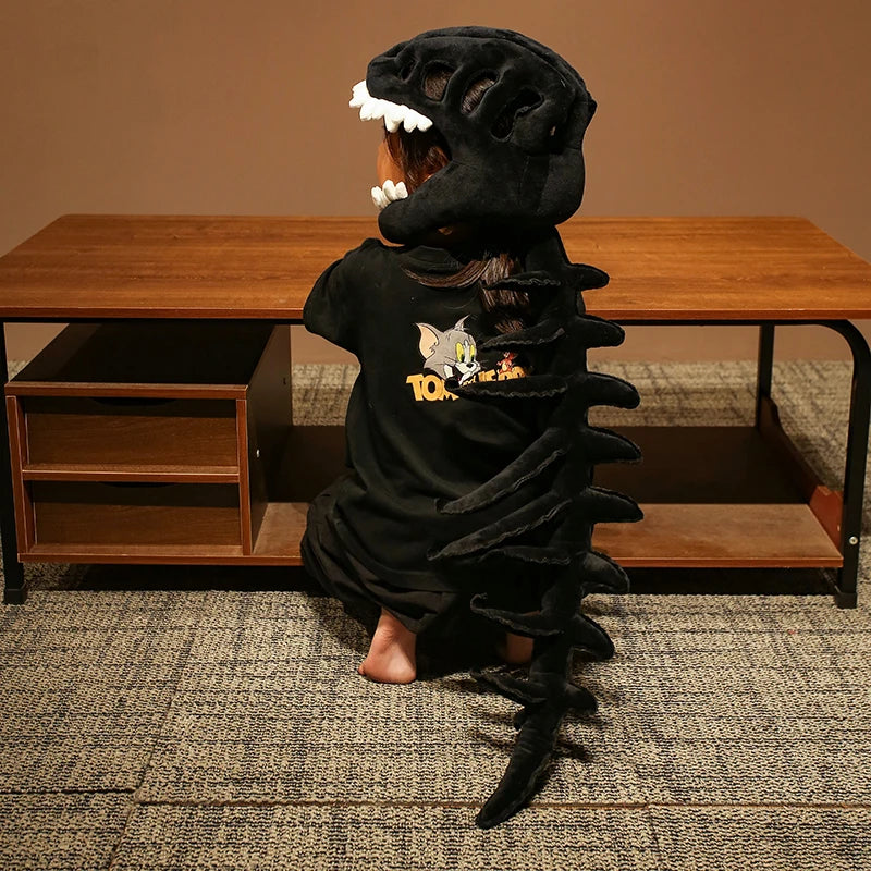 A person wearing a realistic dinosaur skeleton costume with a black headpiece and tail, posing in front of a wooden table.