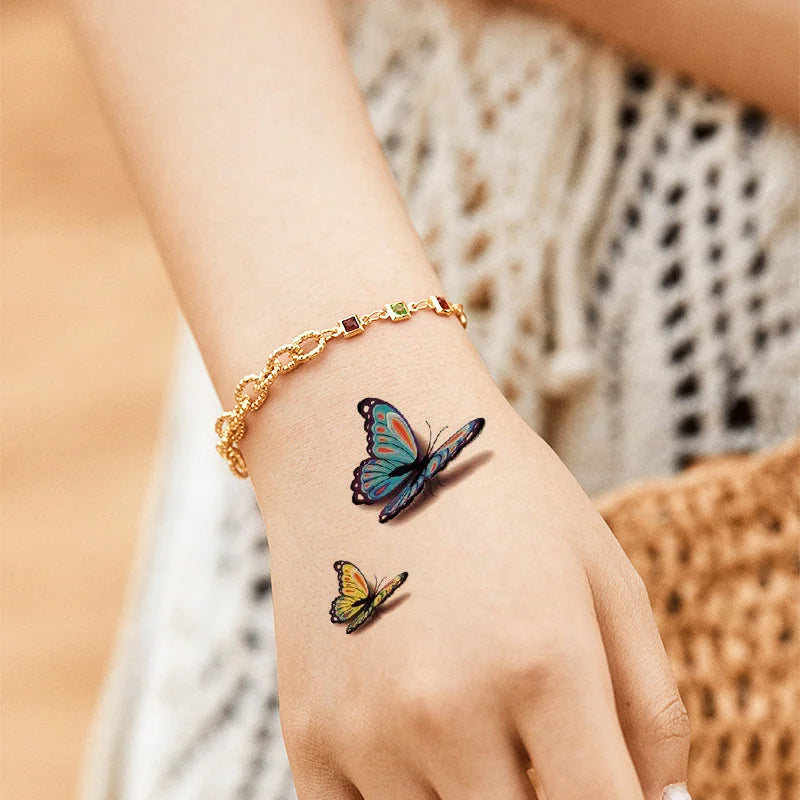 A hand wearing a gold bracelet and displaying temporary body art stickers on the skin.