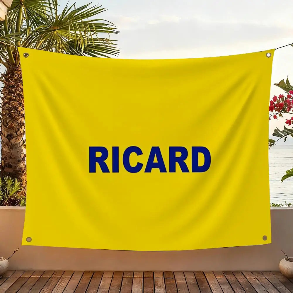A bright yellow flag with the blue text RICARD is displayed outdoors against a backdrop of greenery and water.