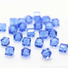 A pile of small, square cut blue glass crystal beads for jewelry making.