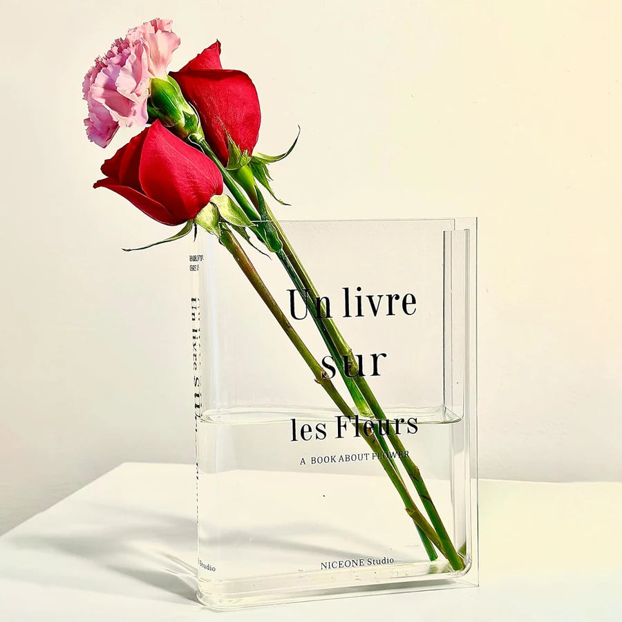 A clear acrylic book vase holds a red rose and a pink carnation.