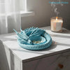 A light blue woven tray filled with gold jewelry and small items, set on a white marble surface.