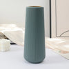 A tall, ribbed, matte sage green plastic vase with a gold rim sitting on a white surface.