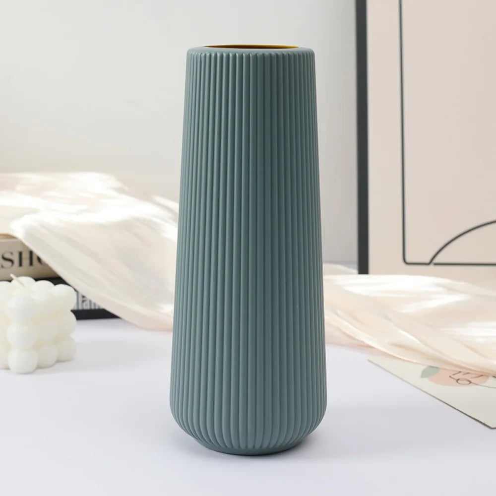 A tall, ribbed, matte sage green plastic vase with a gold rim sitting on a white surface.