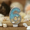 Glitter number cake topper shaped like the number six with a starfish design on a light blue background