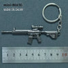 A silver miniature assault rifle model keychain with a keyring attached, shown next to a ruler.