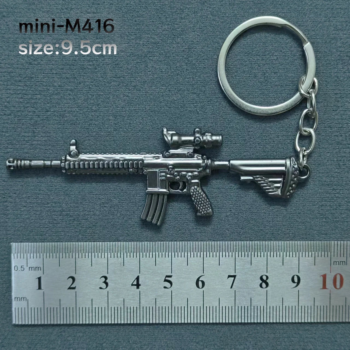 A silver miniature assault rifle model keychain with a keyring attached, shown next to a ruler.