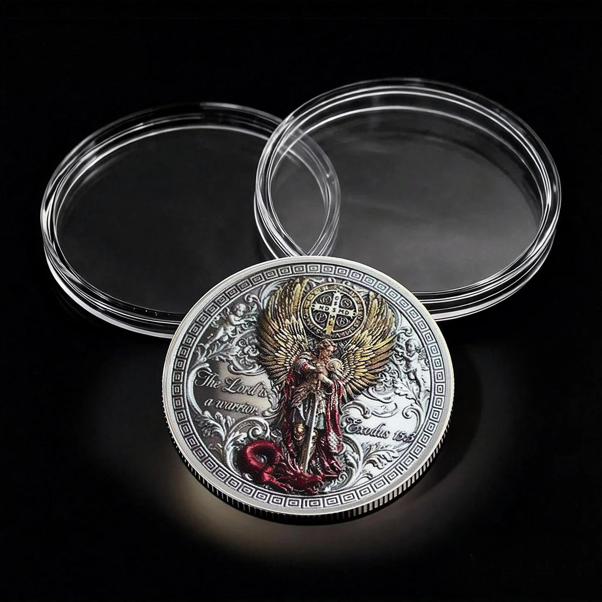 A commemorative coin of Saint Michael the Archangel resting on a black surface with two clear circular containers.