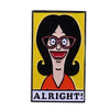 An enamel pin badge featuring a cartoon woman with black hair and glasses against a yellow background, smiling and saying Alr