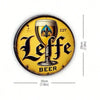 A vintage metal tin sign featuring a stylized Leffe beer glass design on a yellow background.